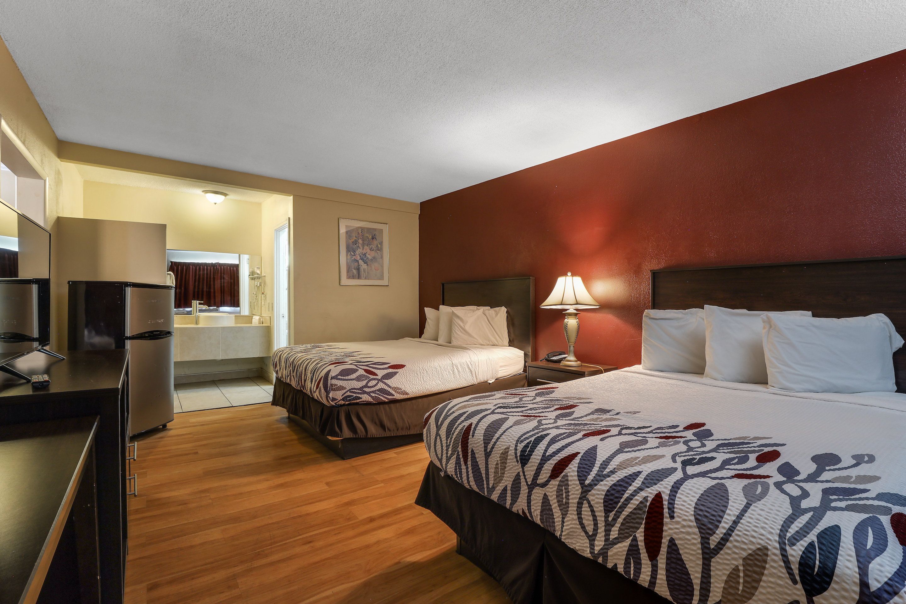 A hotel room with two beds, a desk with a computer, a mirror, and a bathroom visible through an open door.