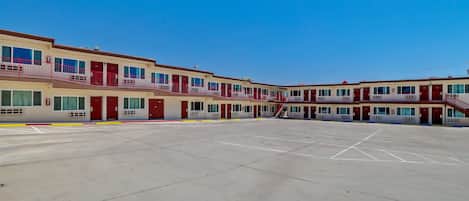 A multi-story motel with a central courtyard, individual rooms with balconies, and a clear blue sky.