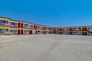 A multi-story motel with a central courtyard, individual rooms with balconies, and a clear blue sky. - Red Roof Inn Needles (Needles)
