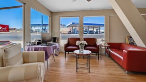 A hotel room with a large window, a ceiling fan, a red sofa, a small table with a vase, and a desk with a computer. - Red Roof Inn Needles (Needles)