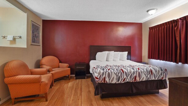 A hotel room with a bed, two armchairs, a nightstand, and a painting on the wall. - Red Roof Inn Needles (Needles)