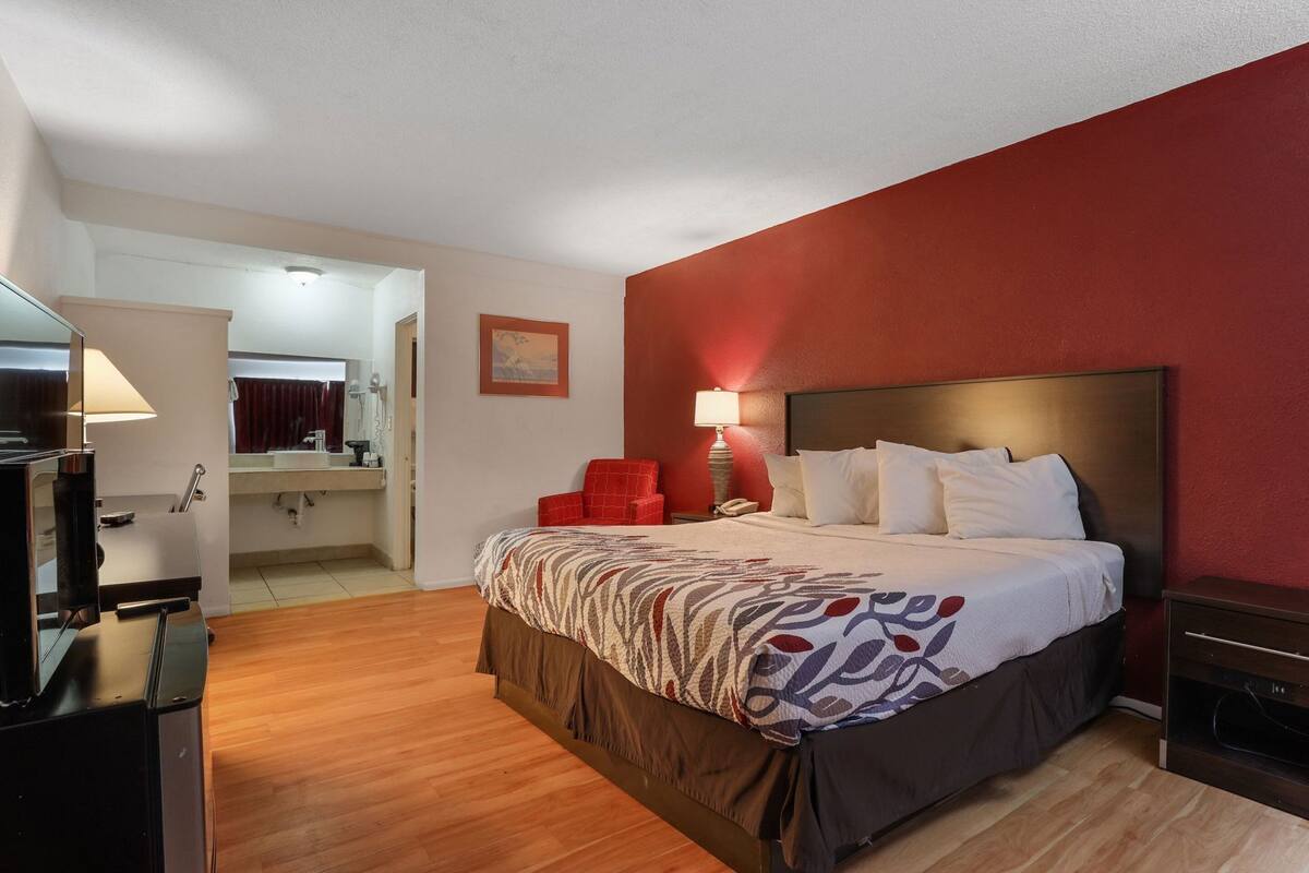 A hotel room with a bed, a desk, a chair, a lamp, and a painting on the wall.