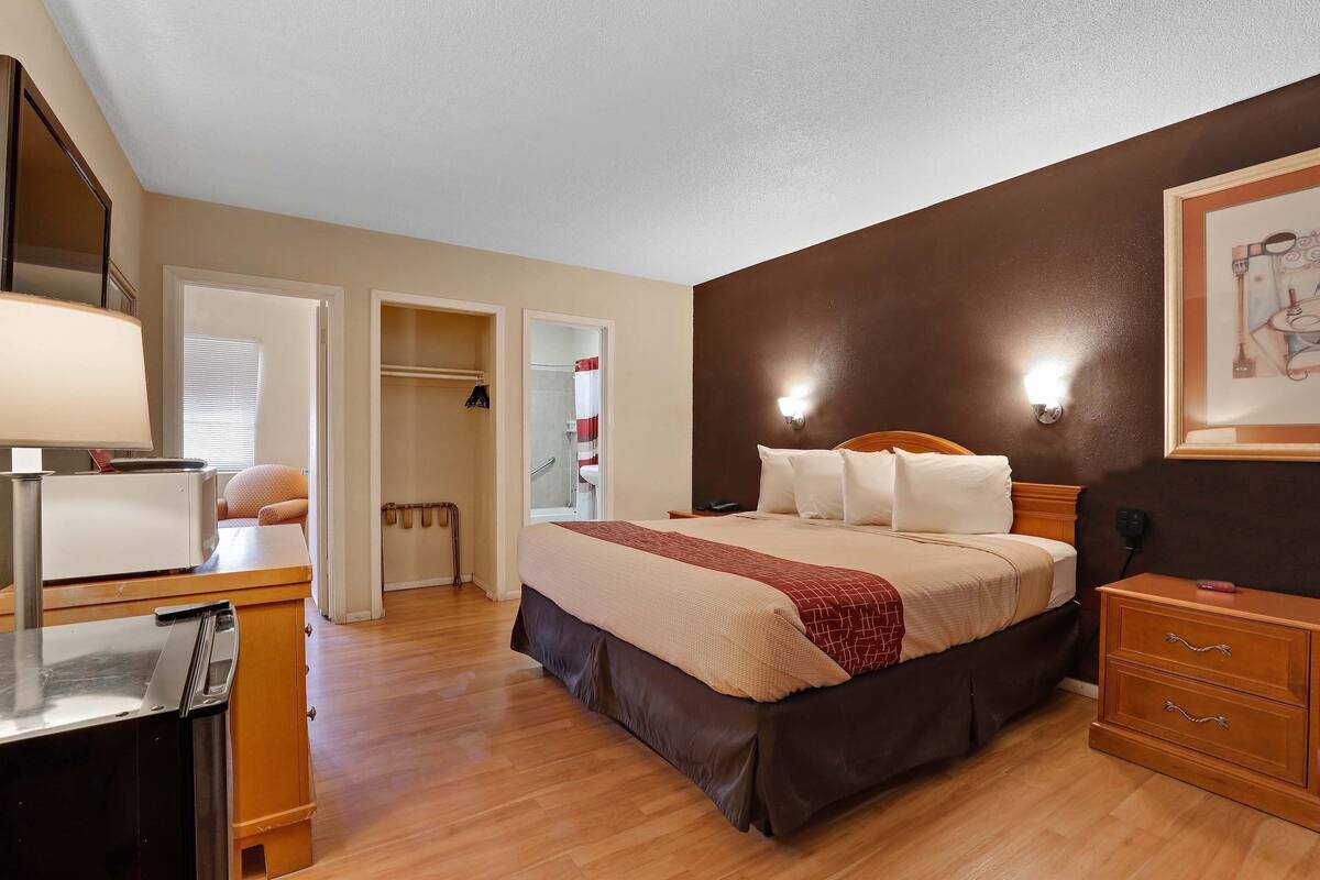 A hotel room with a bed, bedside table, dresser, and a mirror. There is a door leading to a bathroom and a closet.