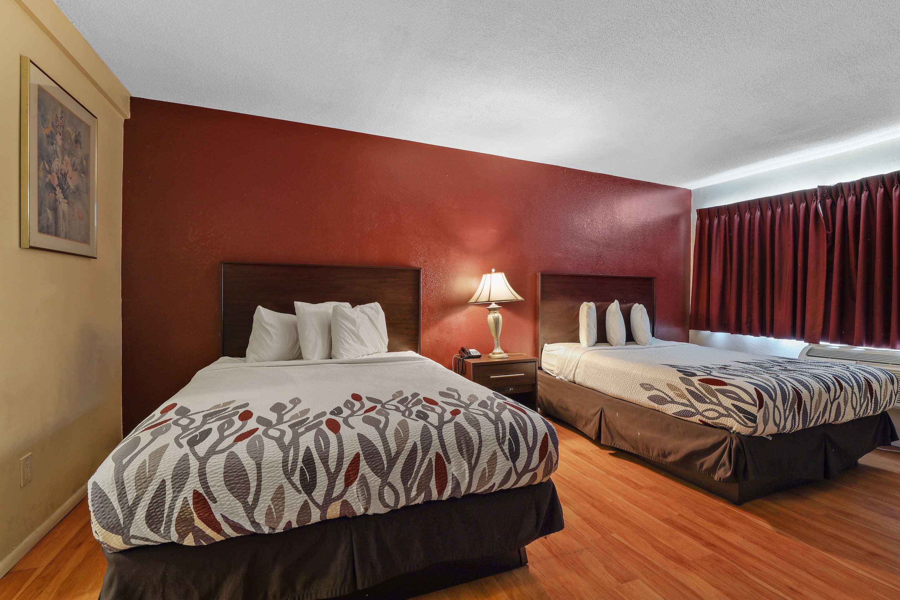 Habitación de hotel con dos camas, una mesita de noche con lámpara y un cuadro en la pared.