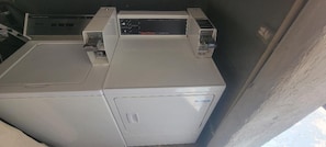 Un electrodoméstico compacto y blanco de estilo industrial, probablemente una lavadora o secadora, con un panel de control y dos asas laterales.