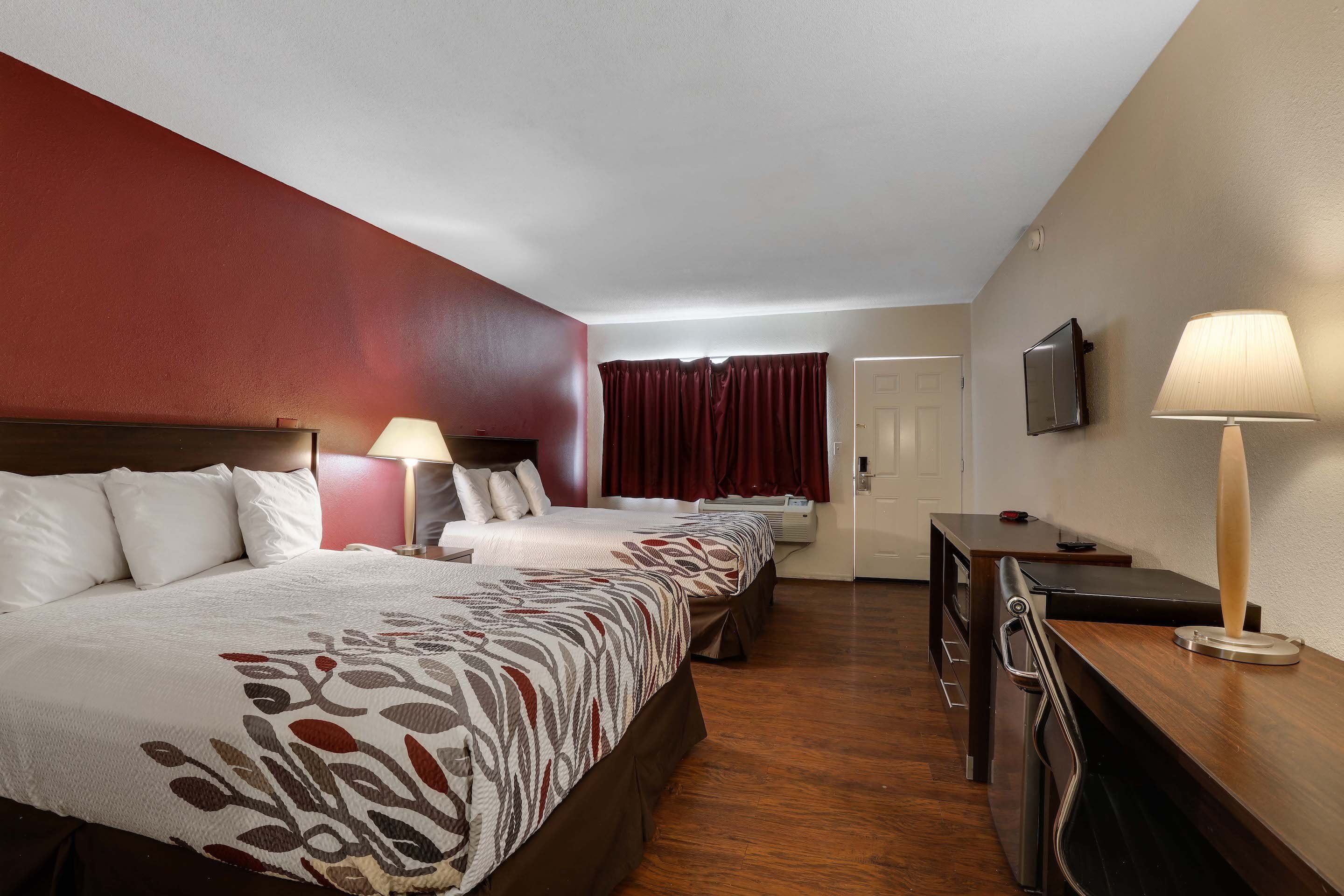 Una habitación de hotel con dos camas, un escritorio, una silla, un televisor y una ventana con cortinas.