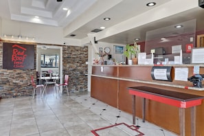 Zona de recepción de Red Roof Inn con pared de piedra, mostrador de recepción y vista al estacionamiento.