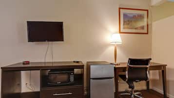 Ein Hotelzimmer mit Schreibtisch, Fernseher, Kühlschrank, Stuhl und Lampe.