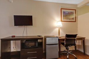 Una habitación de hotel con escritorio, televisor, refrigerador, silla y lámpara.