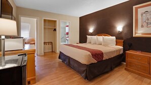 A hotel room with a bed, bedside table, lamp, wardrobe, and a painting on the wall. - Red Roof Inn Needles (Needles)