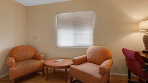 A room with two armchairs, a small round table, a window with blinds, and a lamp. - Red Roof Inn Needles (Needles)