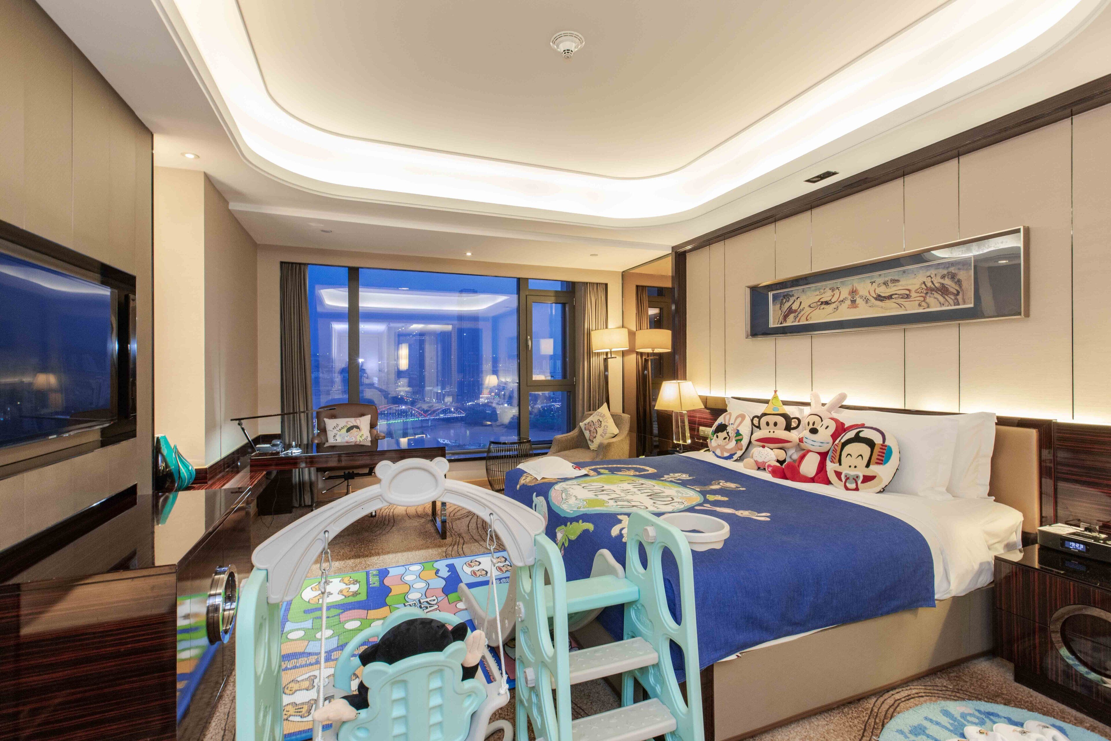 Habitación de hotel con una cama grande, televisión, escritorio y vistas de la ciudad a través de las ventanas.