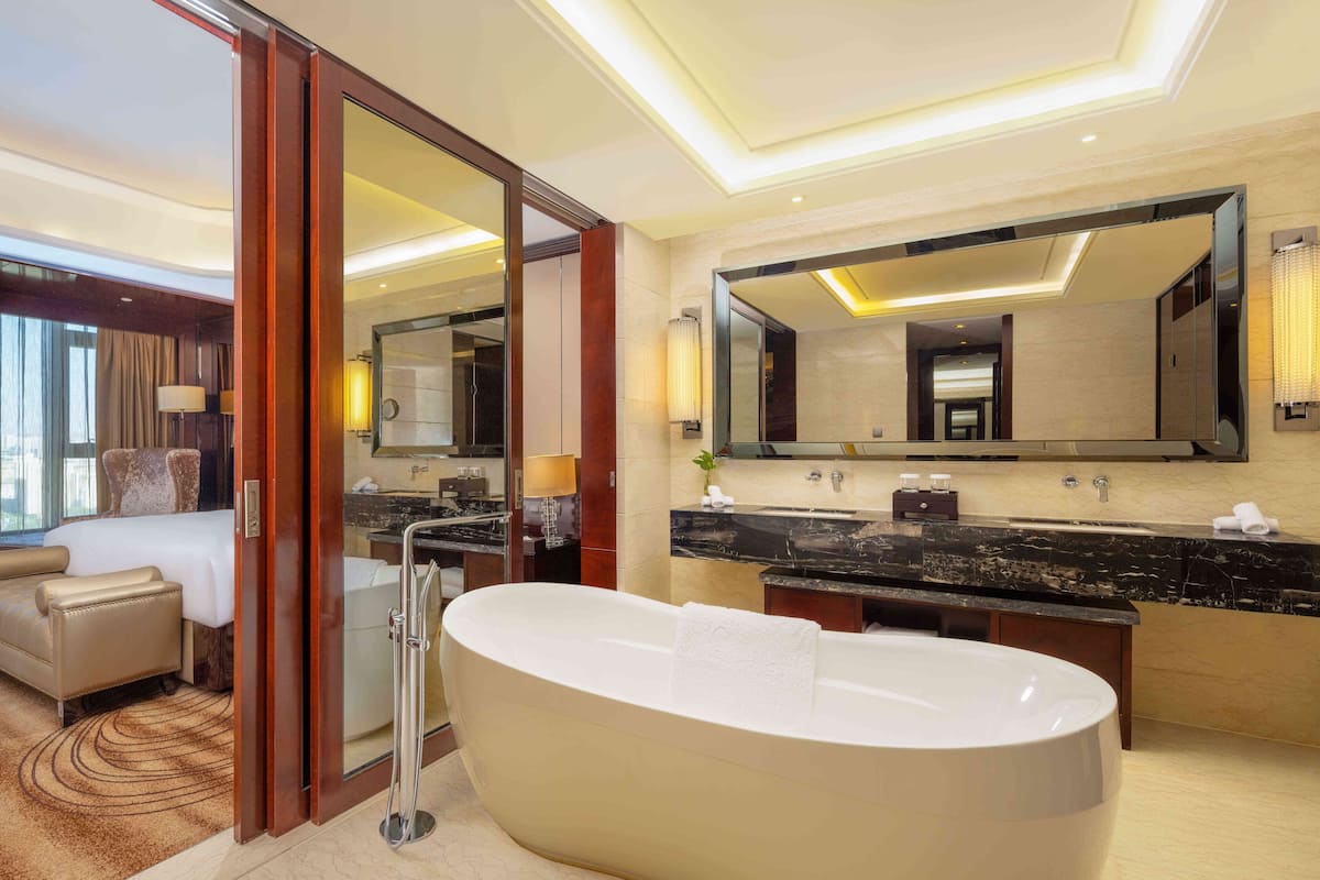 Une salle de bain d’hôtel moderne, dotée d’une grande baignoire sur pieds, d’un meuble-lavabo double avec un plan de travail en marbre noir et d’un grand miroir au-dessus du lavabo.