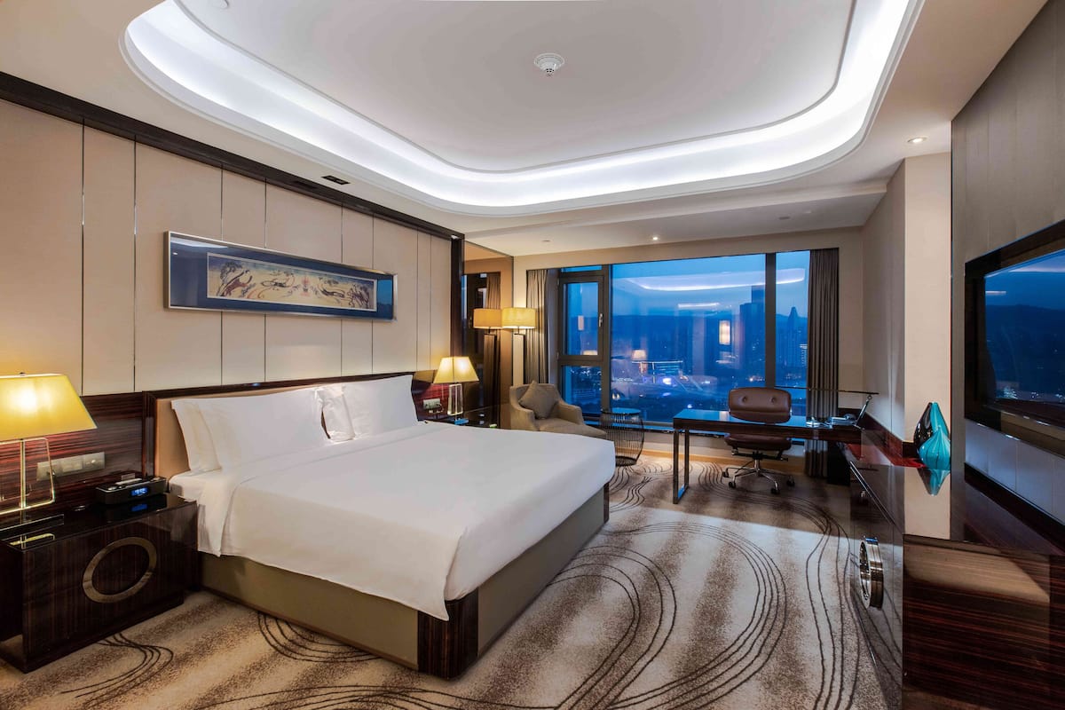 Une chambre d’hôtel moderne dotée d’un grand lit, d’un bureau, d’une chaise et offrant une vue sur le paysage urbain.