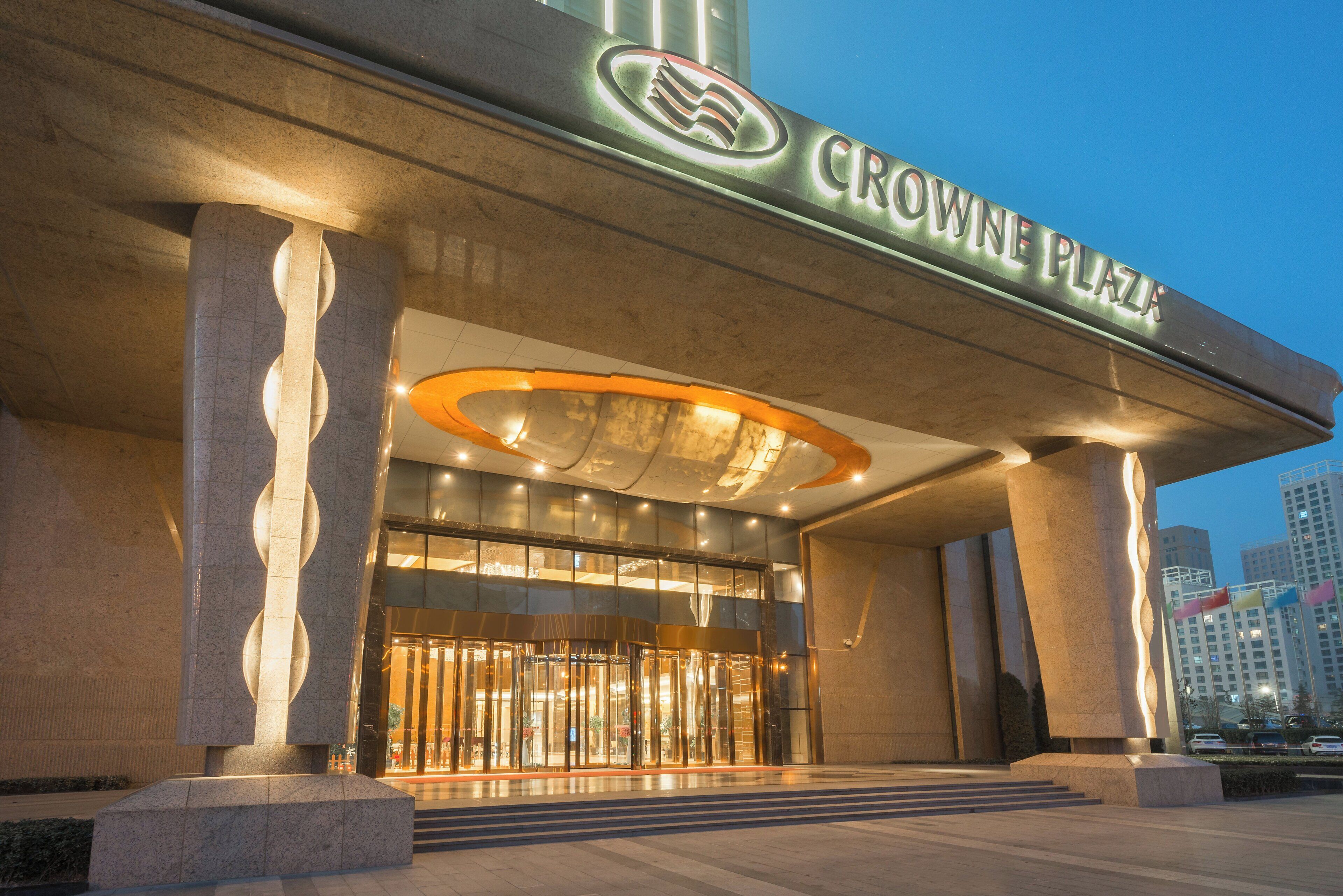 A hotel entrance with a prominent sign reading 'CROWNE PLAZA' and a modern design featuring large columns and a glass facade.