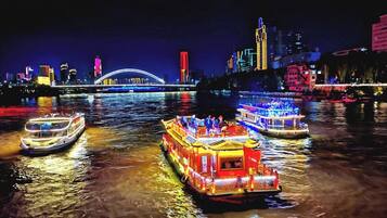 Escena nocturna de un río con barcos iluminados y un puente al fondo.
