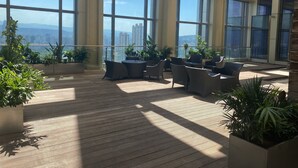 Un balcon spacieux doté de grandes fenêtres, d’un espace salon extérieur et de plantes en pot.