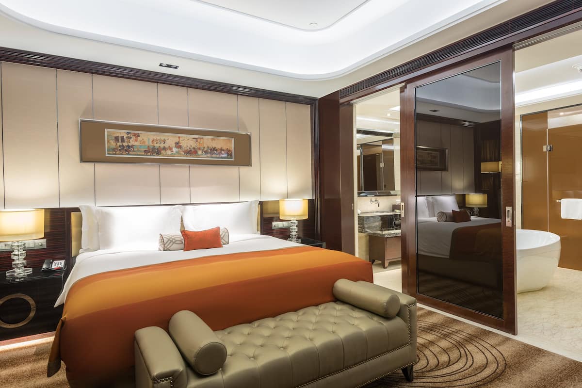 Une chambre d’hôtel avec un grand lit, un canapé, une salle de bain avec baignoire et un miroir.