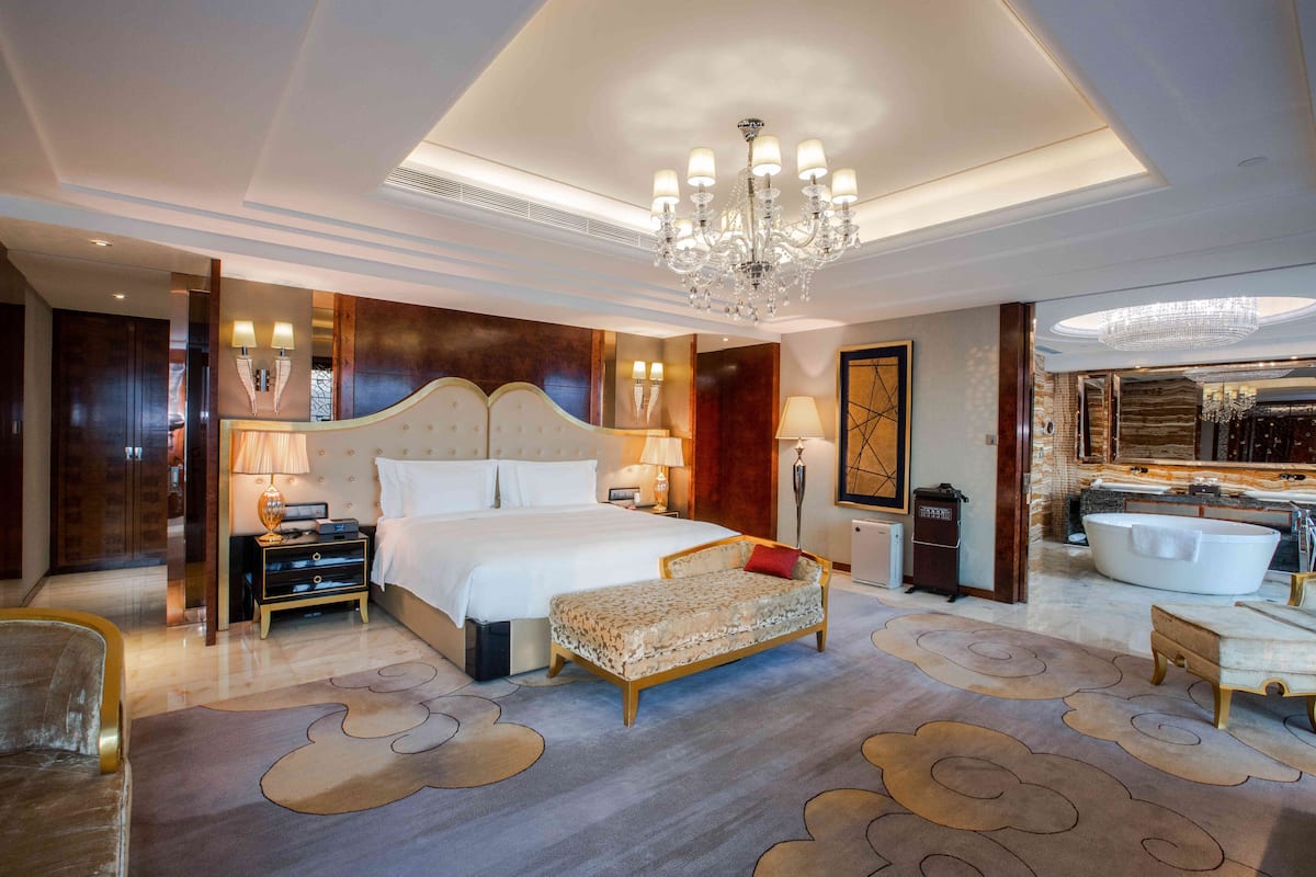 Une chambre spacieuse avec un grand lit, un coin salon, une coiffeuse avec baignoire et un lustre.