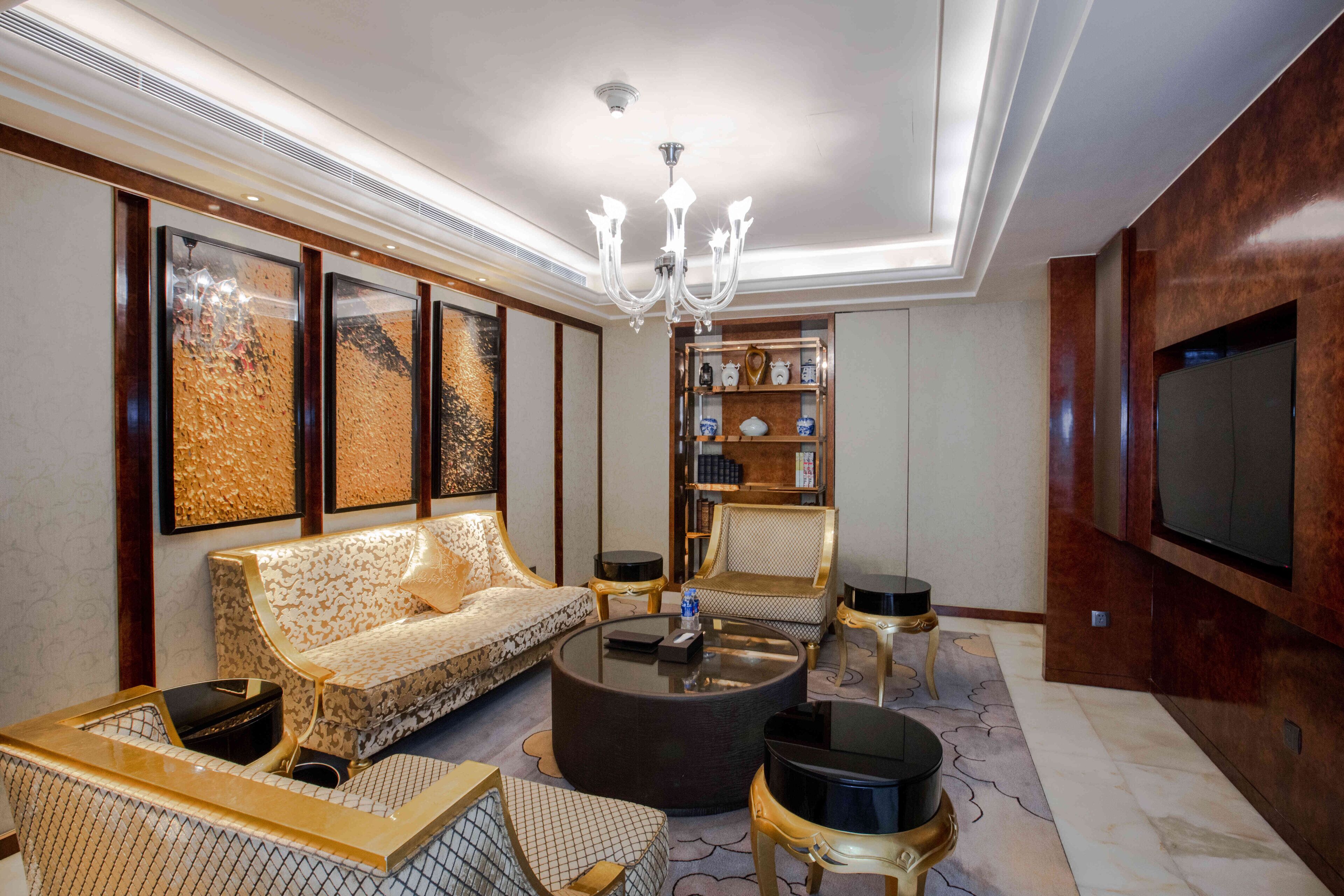A spacious living room with a sofa, armchairs, a coffee table, a bookshelf, and a flat-screen TV mounted on the wall.