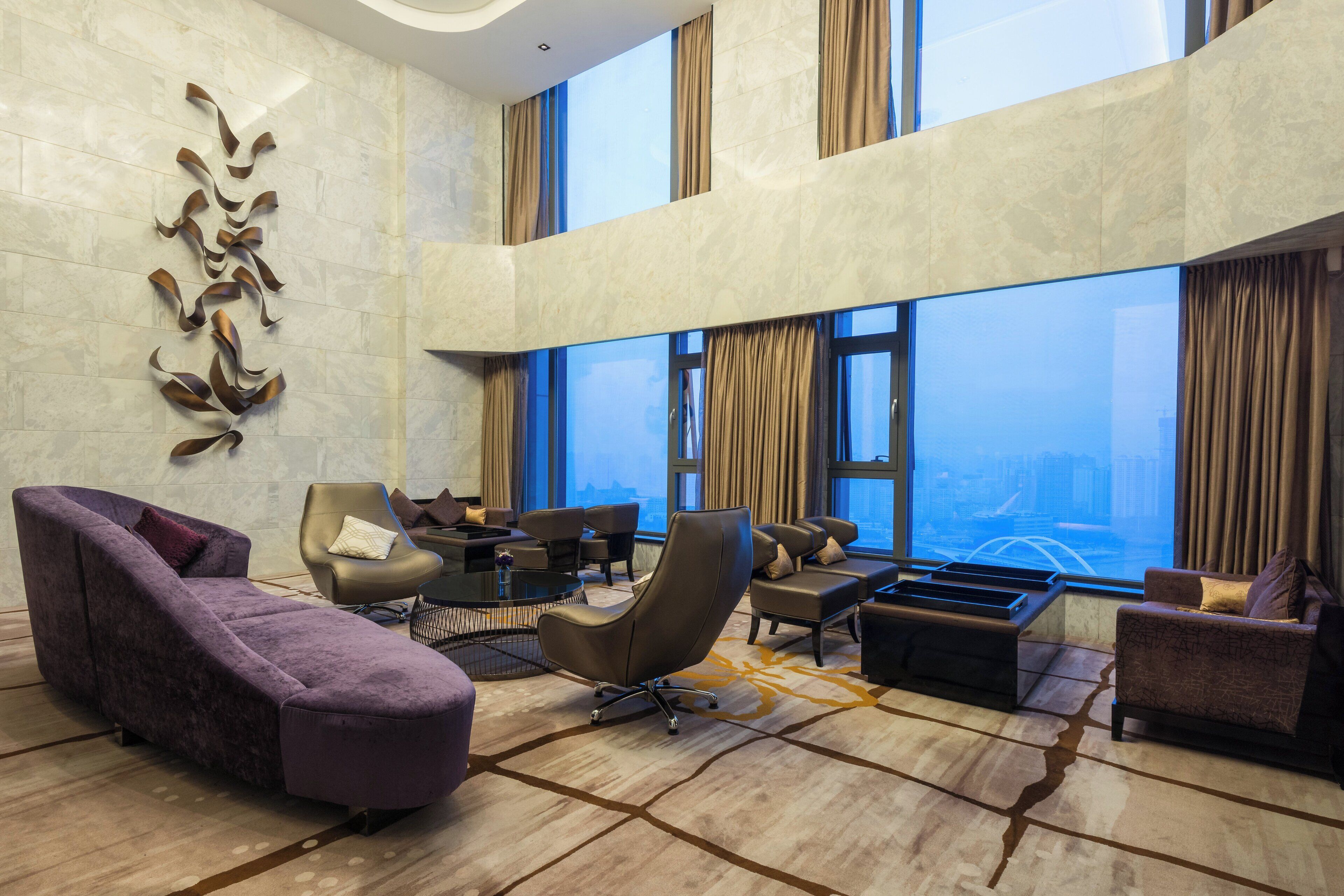 Een ruime lobby met een hoge plafond, moderne meubels en een groot raam met uitzicht over de stad.