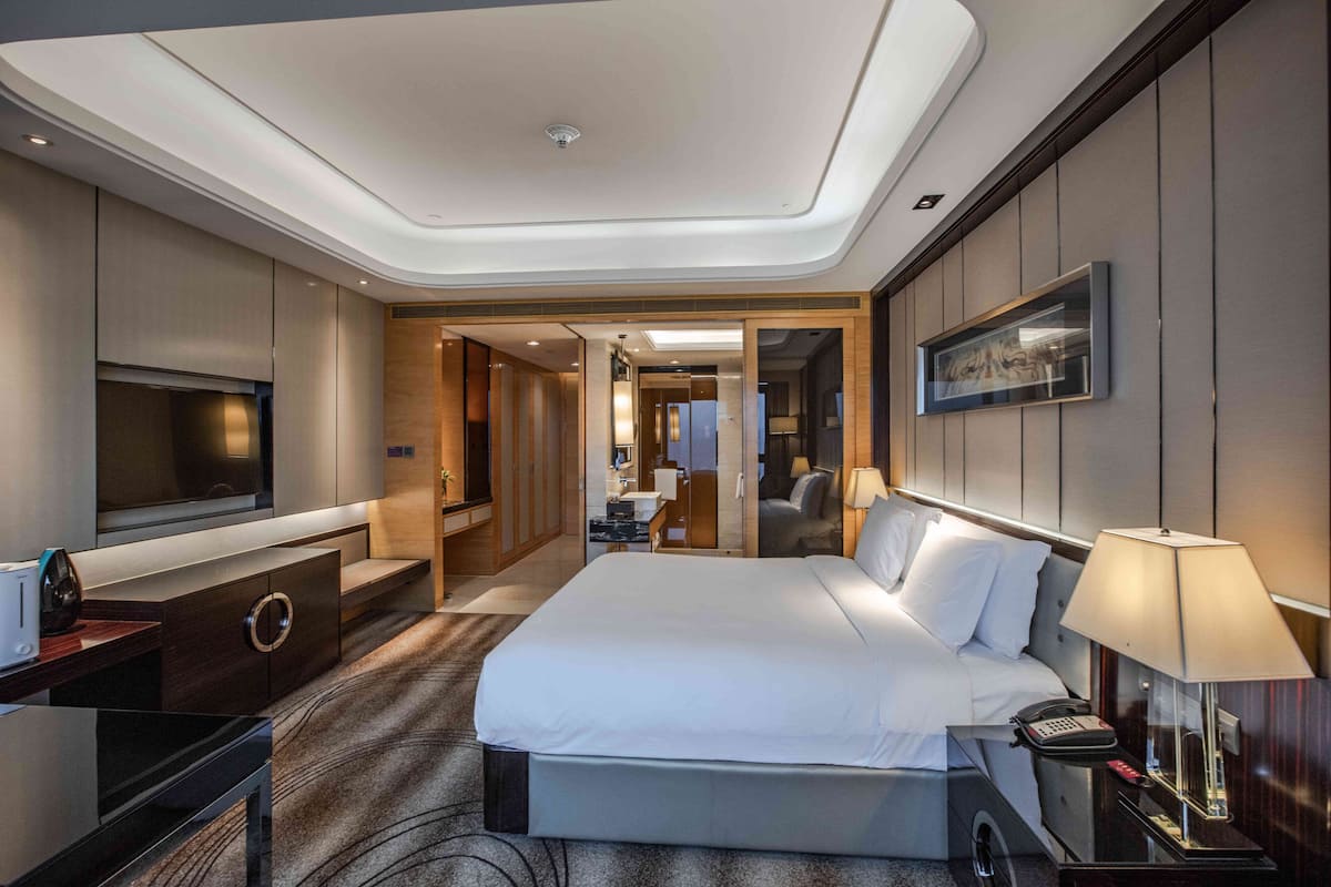 Une chambre d’hôtel moderne dotée d’un grand lit, d’un téléviseur à écran plat, d’un bureau avec une lampe et donnant sur le couloir.