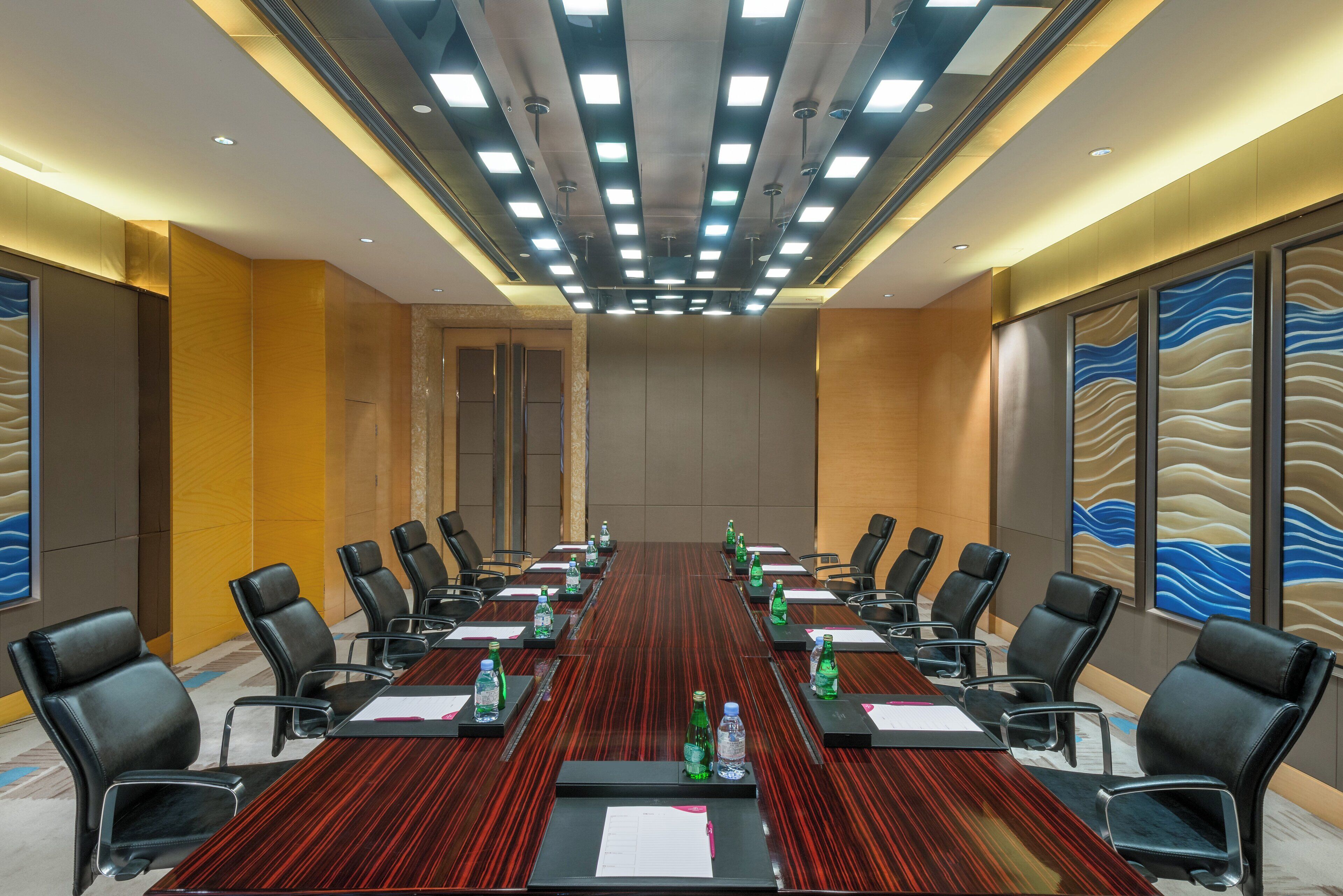 Une salle de conférence avec une longue table, des chaises, des bouteilles d’eau et un grand tableau accroché au mur.