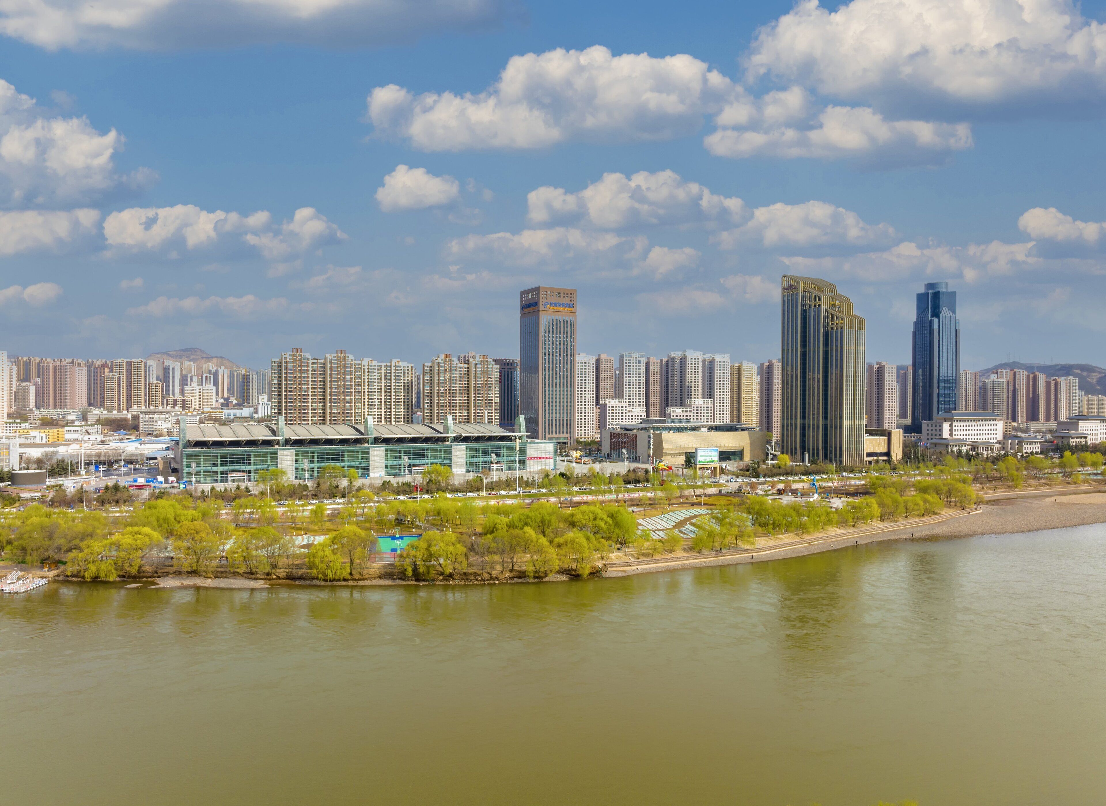 A city skyline with modern high-rise buildings, a river, and a stadium.