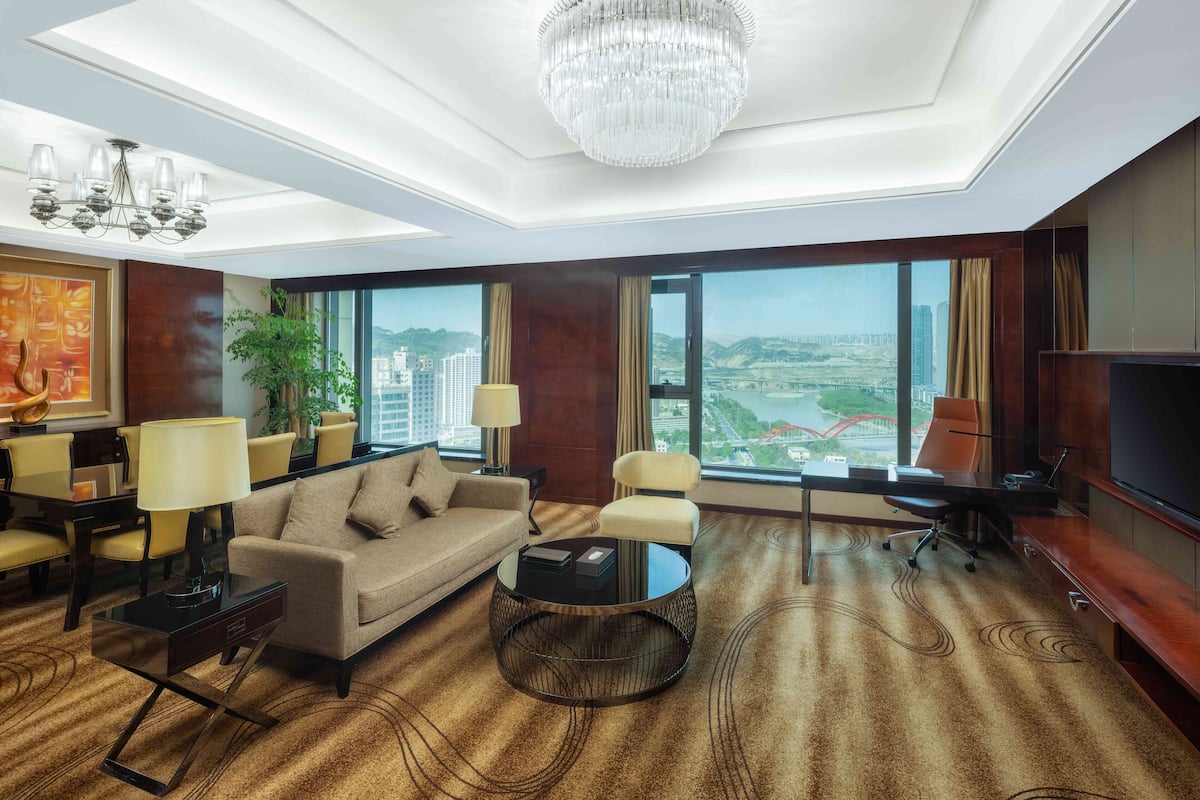 Une chambre d’hôtel moderne dotée d’une grande fenêtre donnant sur la ville, d’un lustre, d’un canapé, d’une table basse et d’un téléviseur.
