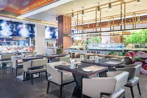 Een modern restaurantinterieur met meerdere eettafels en stoelen, een bar en een vitrine met etenswaren.