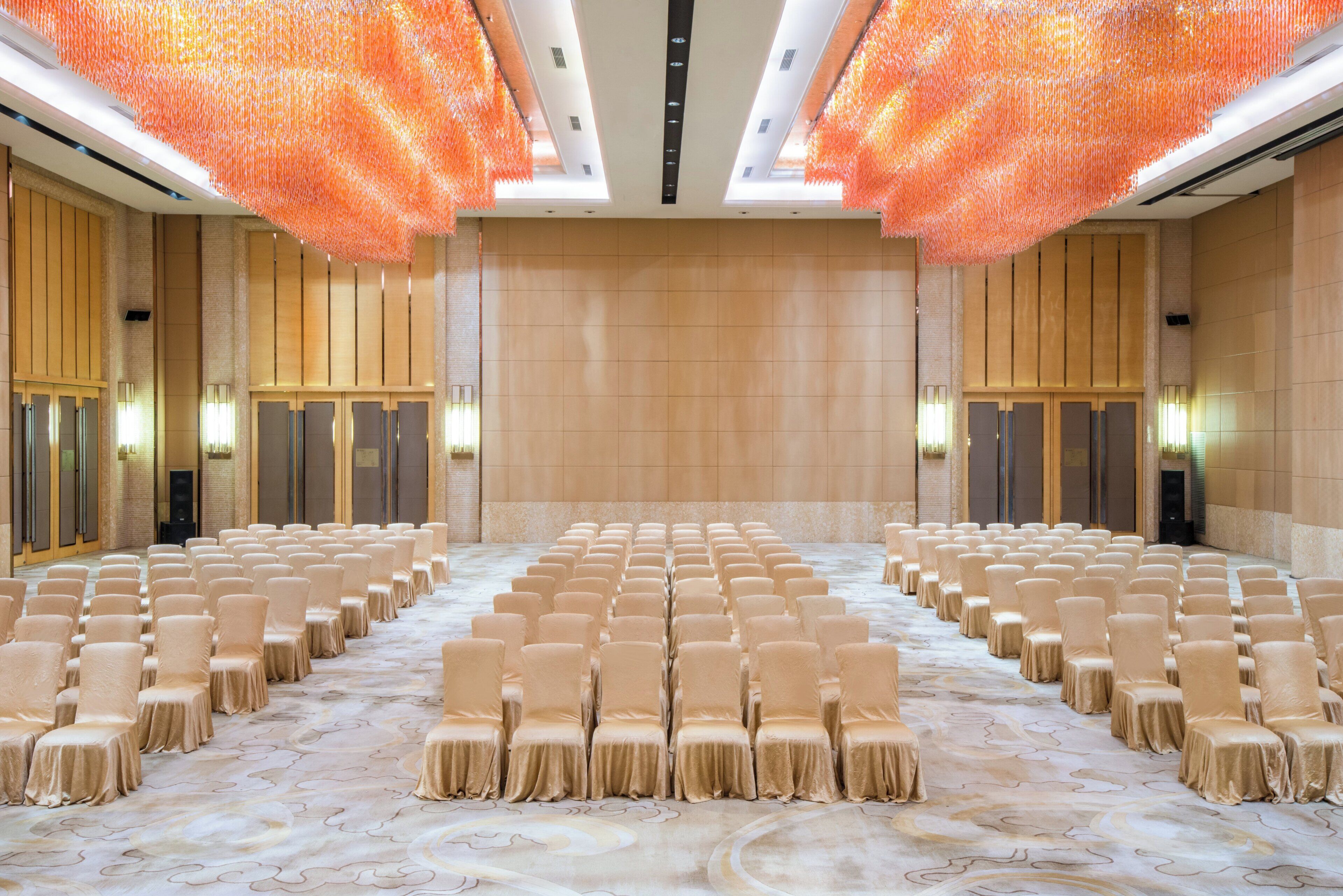 A conference room with rows of chairs, a patterned carpet, and a high ceiling with orange hanging decorations.