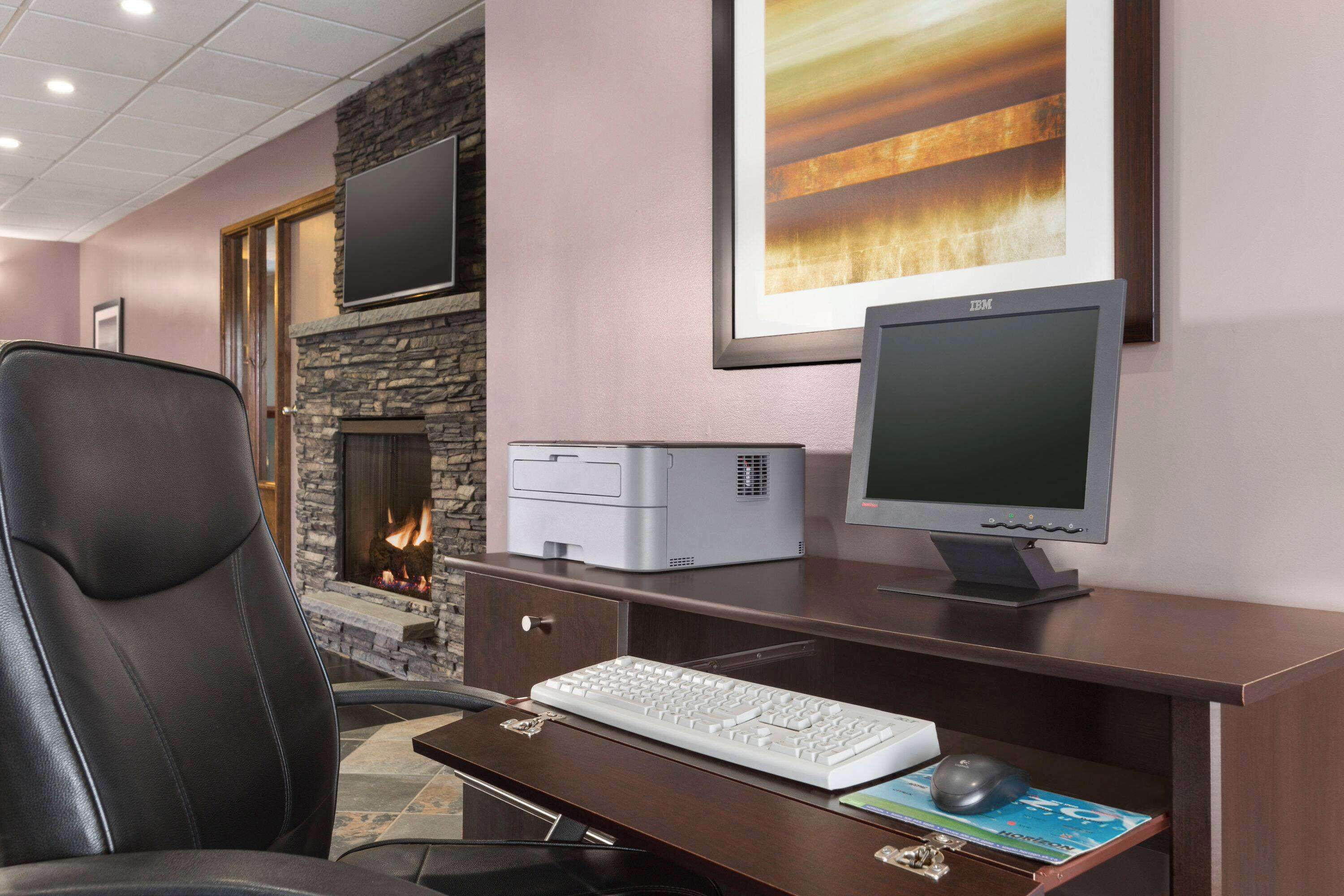 Habitación de hotel con chimenea, escritorio, computadora, teclado, ratón y una silla.
