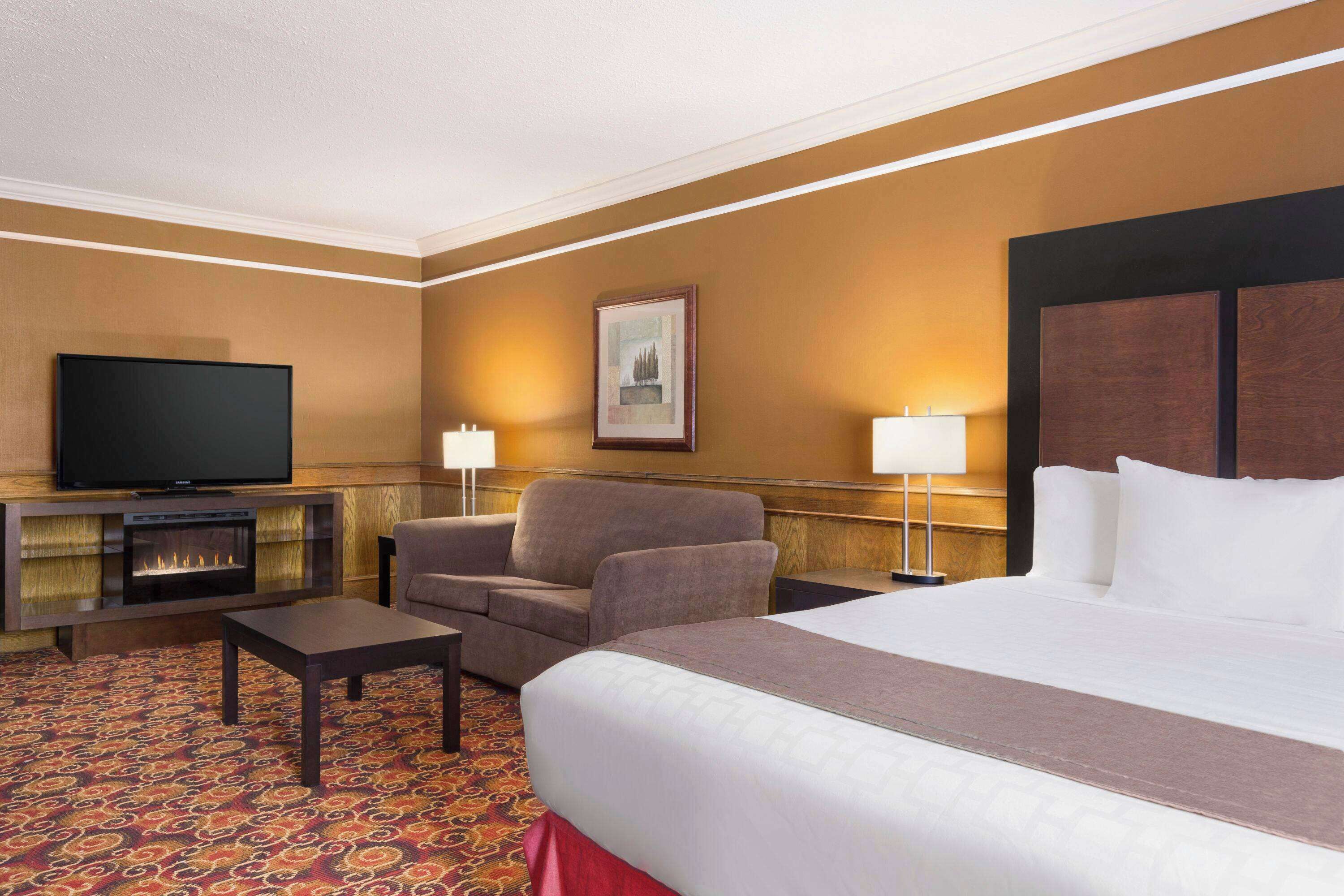 Habitación de hotel con una cama grande, televisión, chimenea, sofá y dos lámparas.