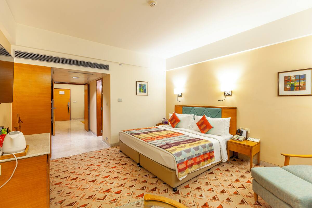 A hotel room with a large bed, bedside tables, a chair, and a desk with a computer.