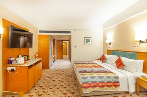 Habitación de hotel con cama, mesita de noche, televisor y escritorio con silla.