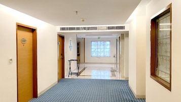 Un pasillo de hotel con piso de diseño azulado, puertas de madera y una ventana con motivos decorativos.