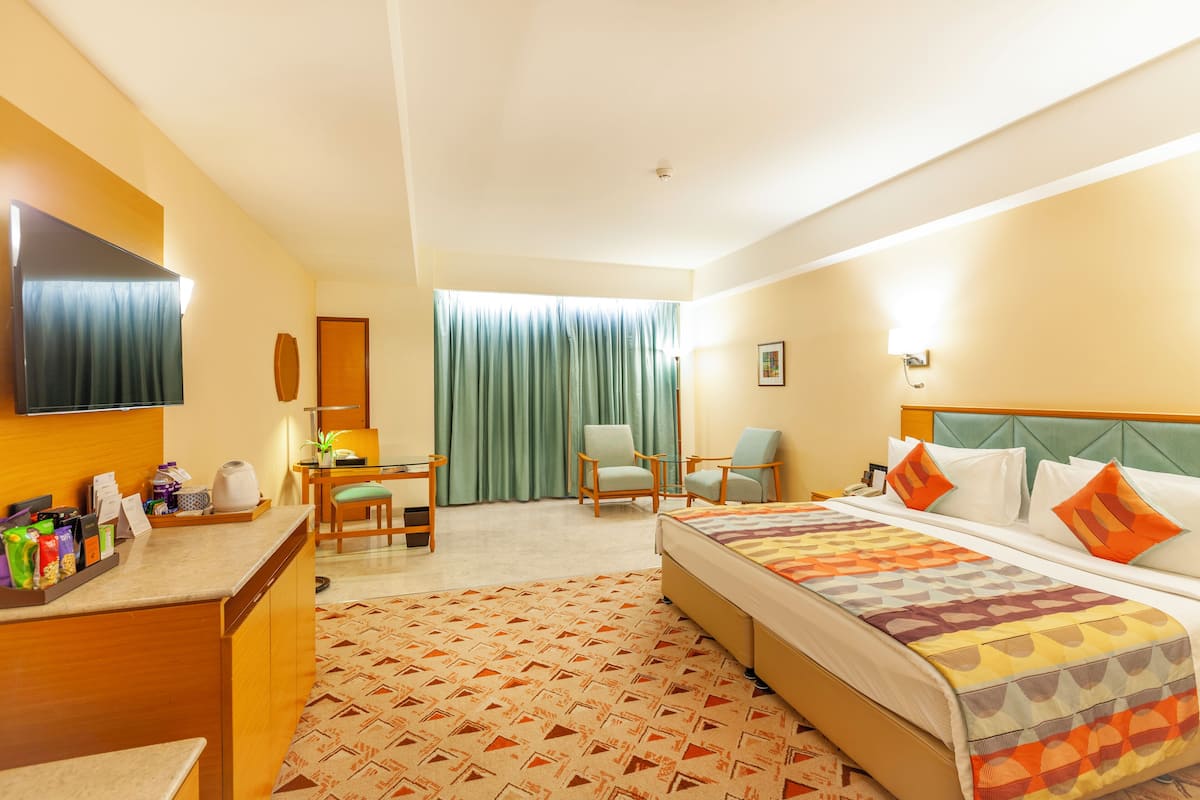 A hotel room with a bed, a desk, a chair, a television, and a window with curtains.