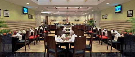 A spacious restaurant with multiple dining tables and booths, a high ceiling with recessed lighting, and wall-mounted televisions.