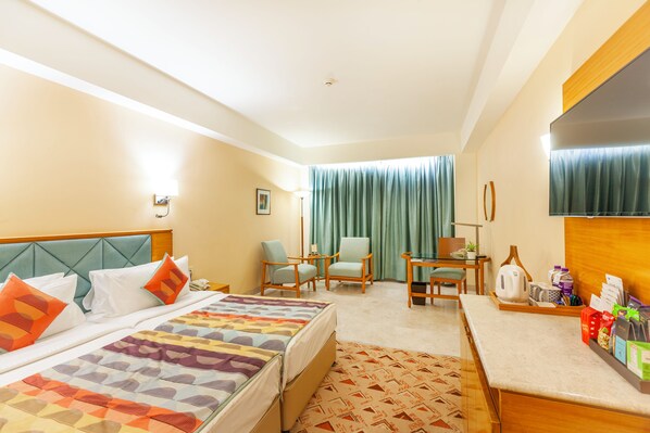 A hotel room with a bed, two chairs, a desk, a TV, and a window with curtains.