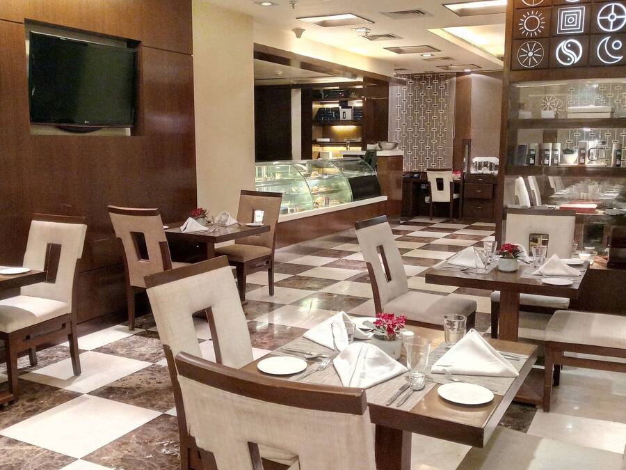 Un restaurante con suelo a cuadros, mesas y sillas de madera, y una vitrina en el fondo.