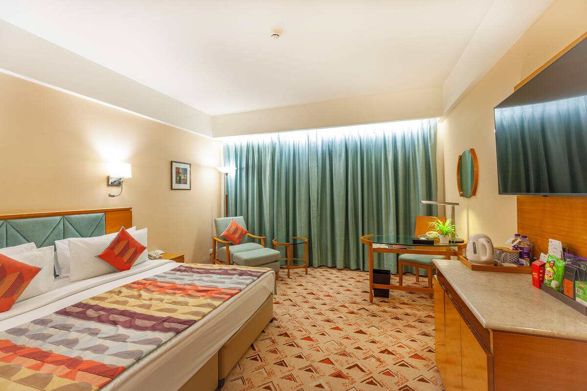 A hotel room with a bed, a desk, a chair, a coffee machine, and a TV.
