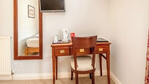 Habitación de hotel con un escritorio de madera, una silla, un televisor montado en la pared, un espejo y un radiador.