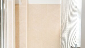 Une petite salle de bain moderne, équipée de toilettes, d’un radiateur et d’une fenêtre avec des stores.