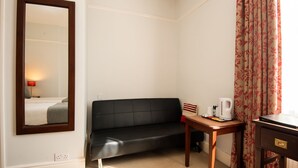 Habitación de hotel con sofá de cuero negro, una mesita de madera con tetera, un espejo y una ventana con cortinas.