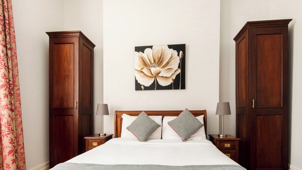 Un dormitorio con una cama grande, dos mesitas de noche, un armario de madera y una obra de arte floral en la pared.