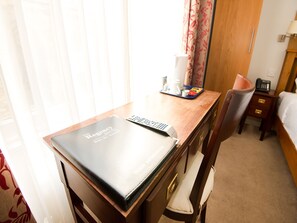 A hotel room with a wooden desk, a black folder labeled "The Regency Bristol Hotel - Bar Restaurant," a remote control, a tray with a coffee pot, a phone, and a bedside table with a lamp. - Oyo The Regency (Bristol)