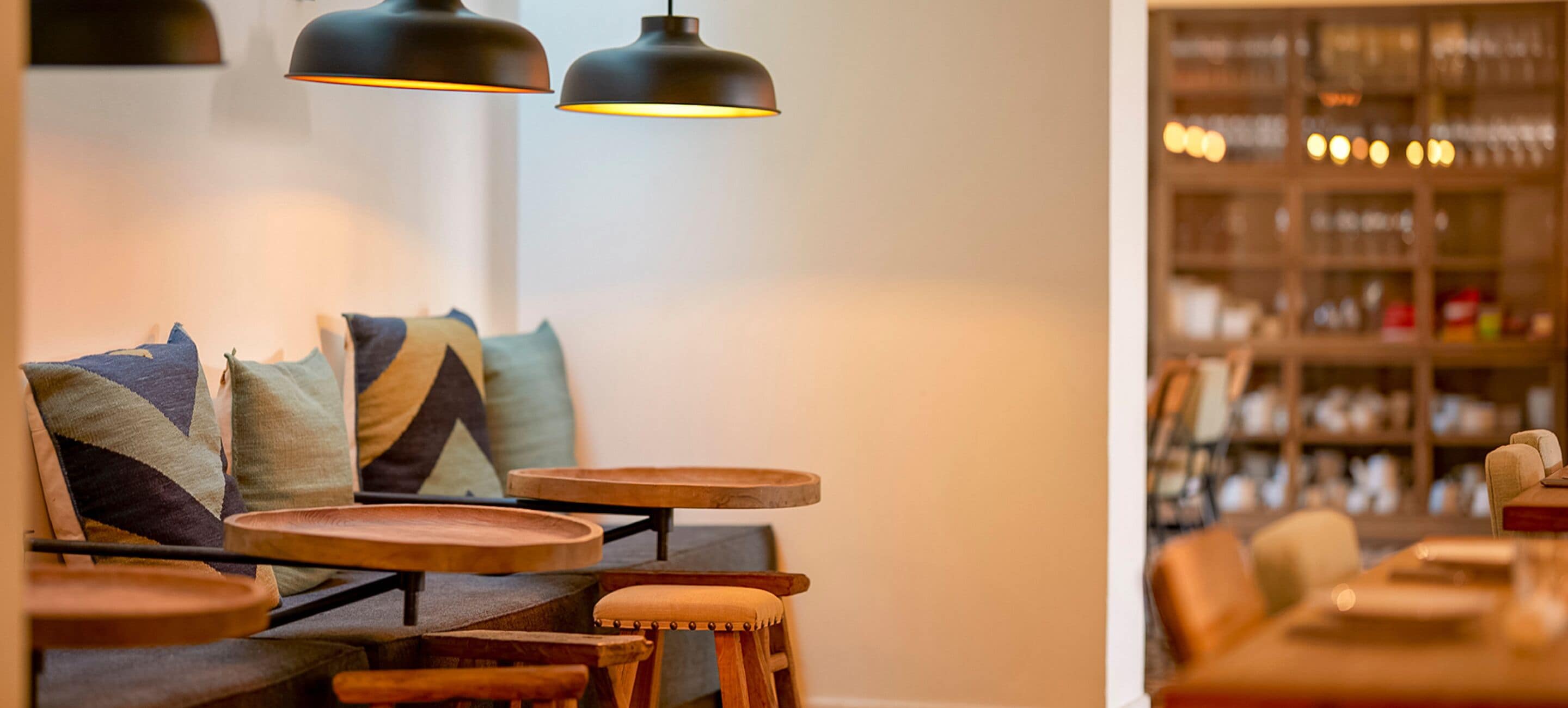 Un coin salon accueillant avec un canapé, plusieurs tables en bois et des lampes suspendues.
