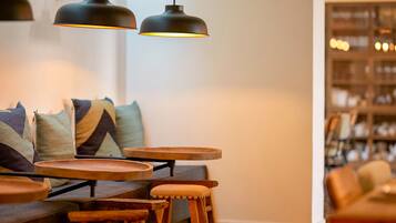 Un coin salon accueillant avec un canapé, plusieurs tables en bois et des lampes suspendues.