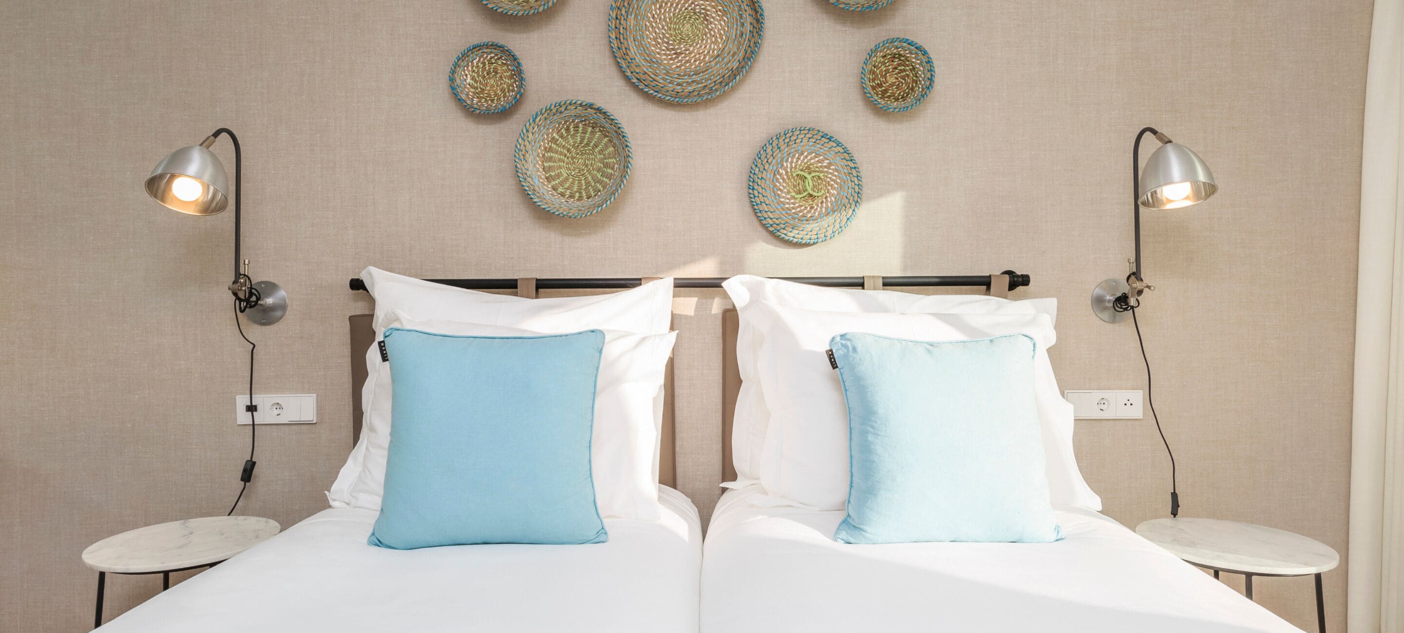 Una cama doble con almohadas blancas y azul claro, dos mesitas de noche y lámparas fijadas a la pared.
