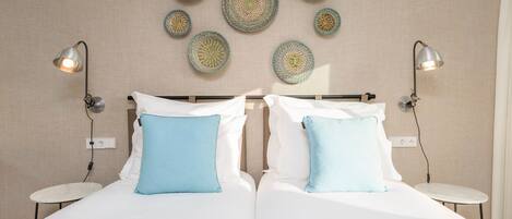 A double bed with white and light blue pillows, two bedside tables, and wall-mounted lamps.